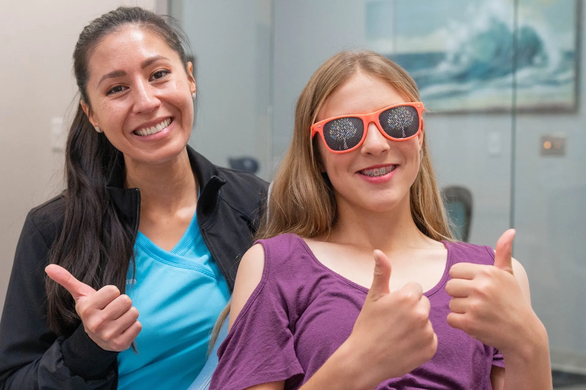 Smiling orthodontic patient with braces and sunglasses giving thumbs up alongside a staff member at St. Johns Orthodontics, promoting a friendly and supportive environment for orthodontic care.