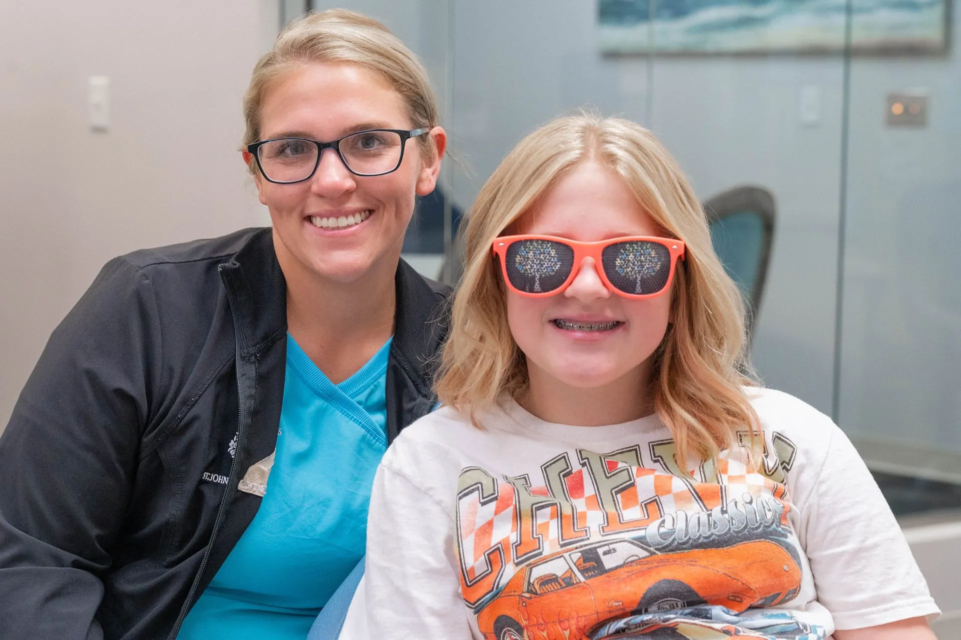 Smiling orthodontist and child with braces wearing colorful sunglasses, showcasing a positive dental experience at St. Johns Orthodontics.
