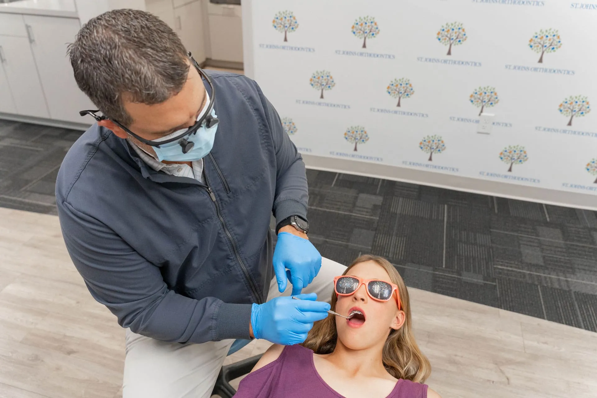 Orthodontist examining a teenage girl wearing sunglasses during a braces consultation at St. Johns Orthodontics, promoting confidence and proper jaw alignment.